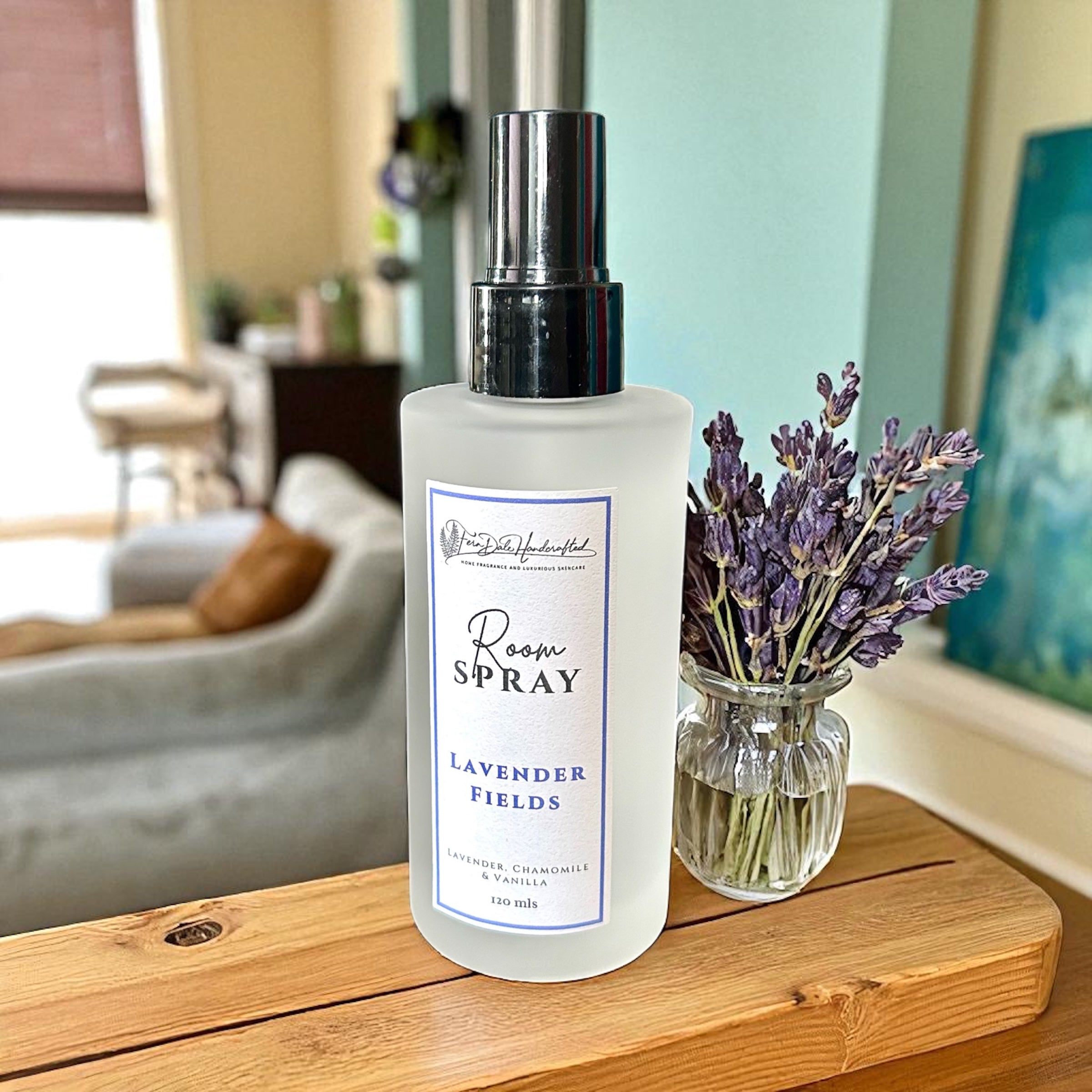 Room Sprays frosted bottle with a silver cap beside a glass vase of dried lavender on a wooden surface.