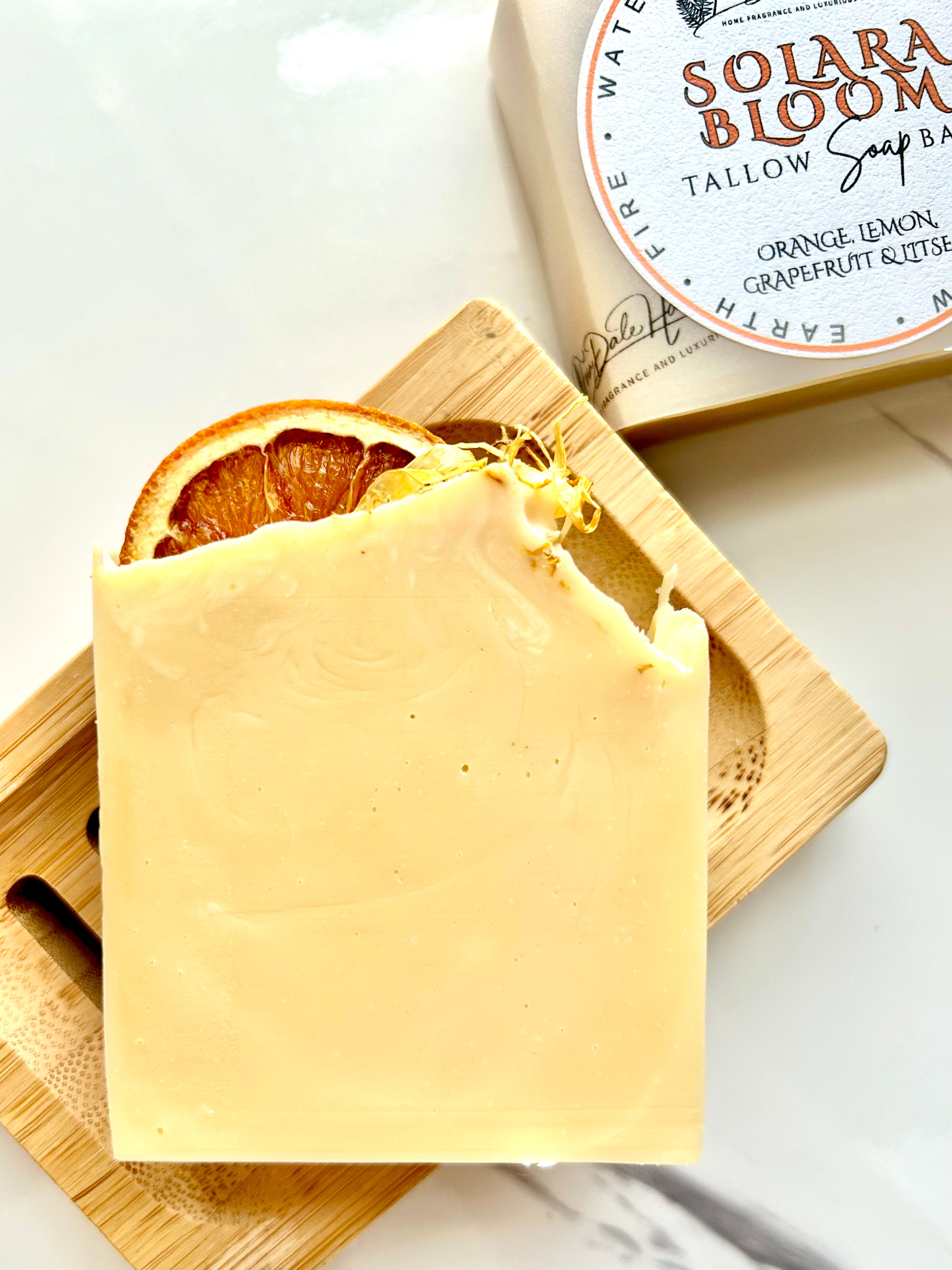 Solara Bloom - Orange, Grapefruit, Lemon & Litsea (Sun) Tallow Soap on a wooden dish with a dried orange slice.