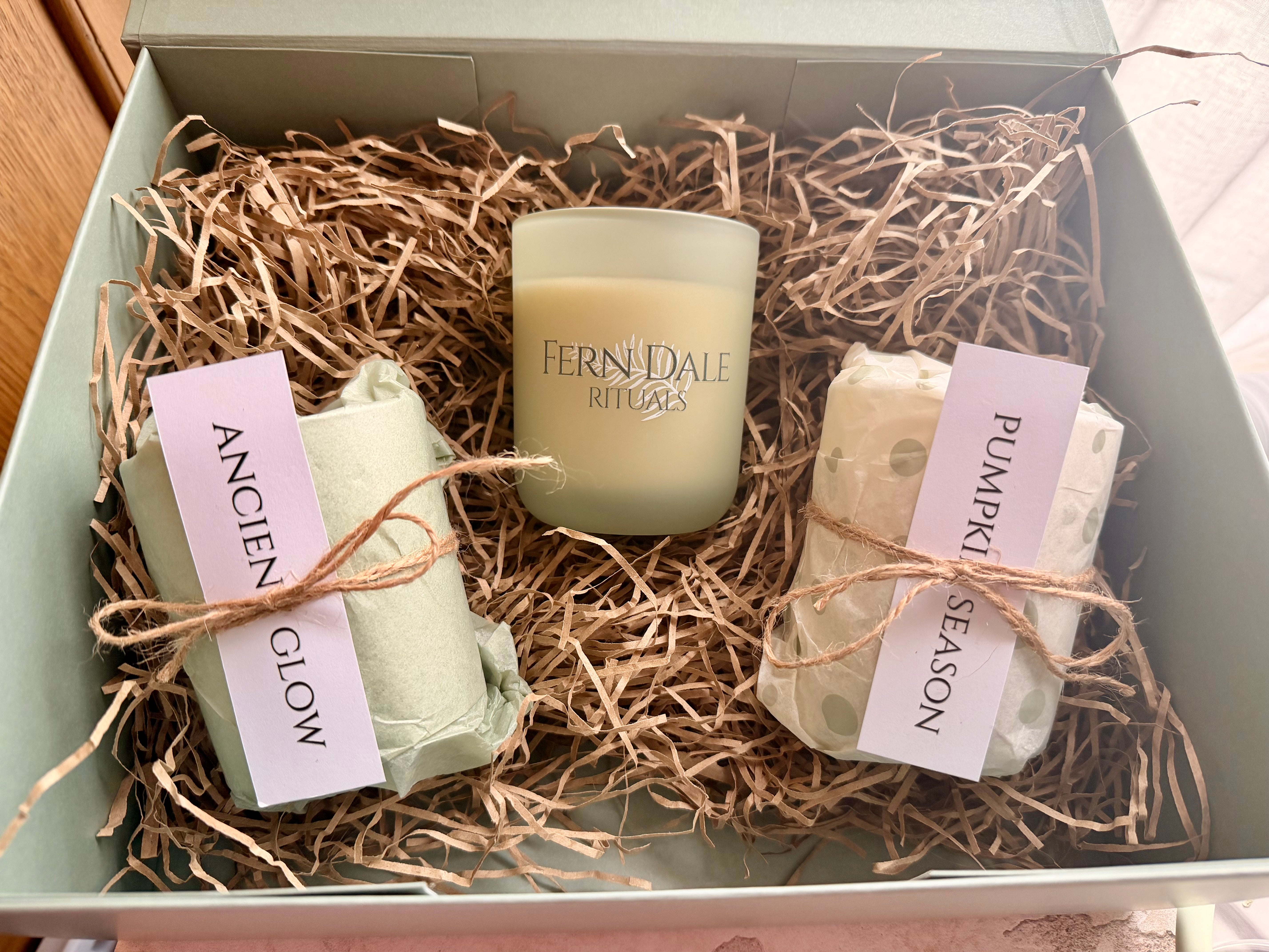 The Candle Ritual Gift Set in an open green box with a frosted candle jar, twine-tied parcels and shredded paper.